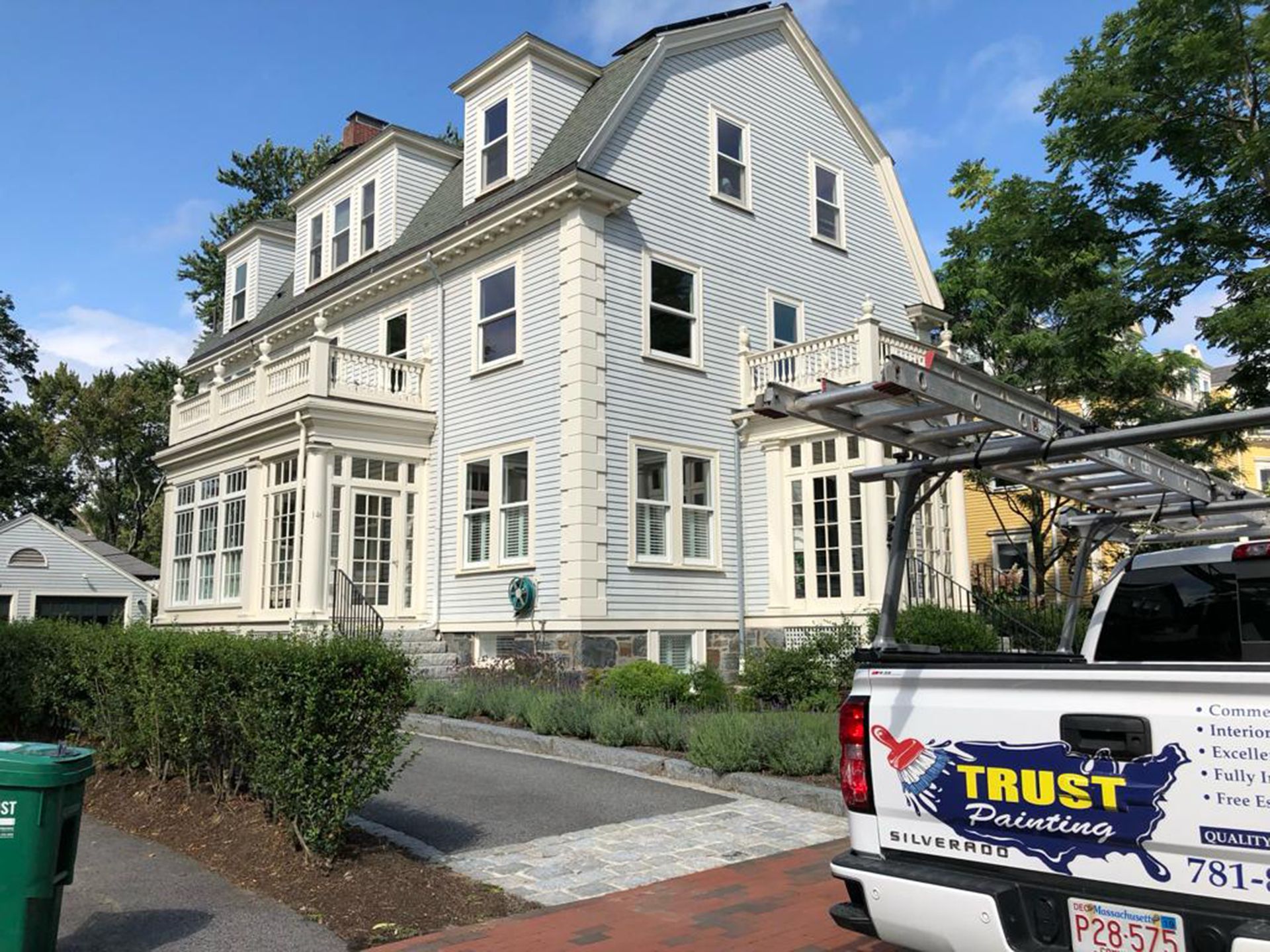 A white house with a gambrel roof viewed from the street, next to a Trust Painting service truck.