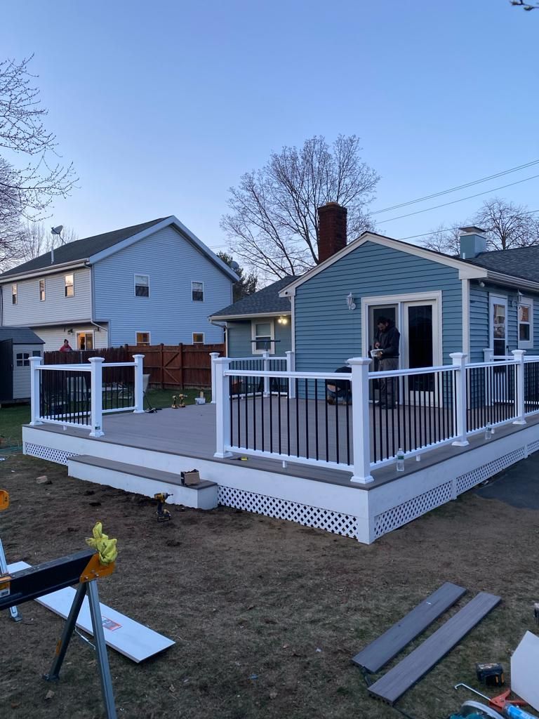A newly constructed deck with white railings and black balusters attached to a blue house in a backyard at dusk.