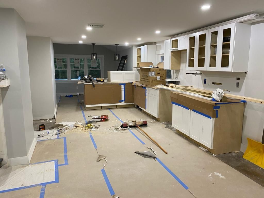 A kitchen undergoing renovation with white cabinets, wood-topped counters, and blue tape on the floor.