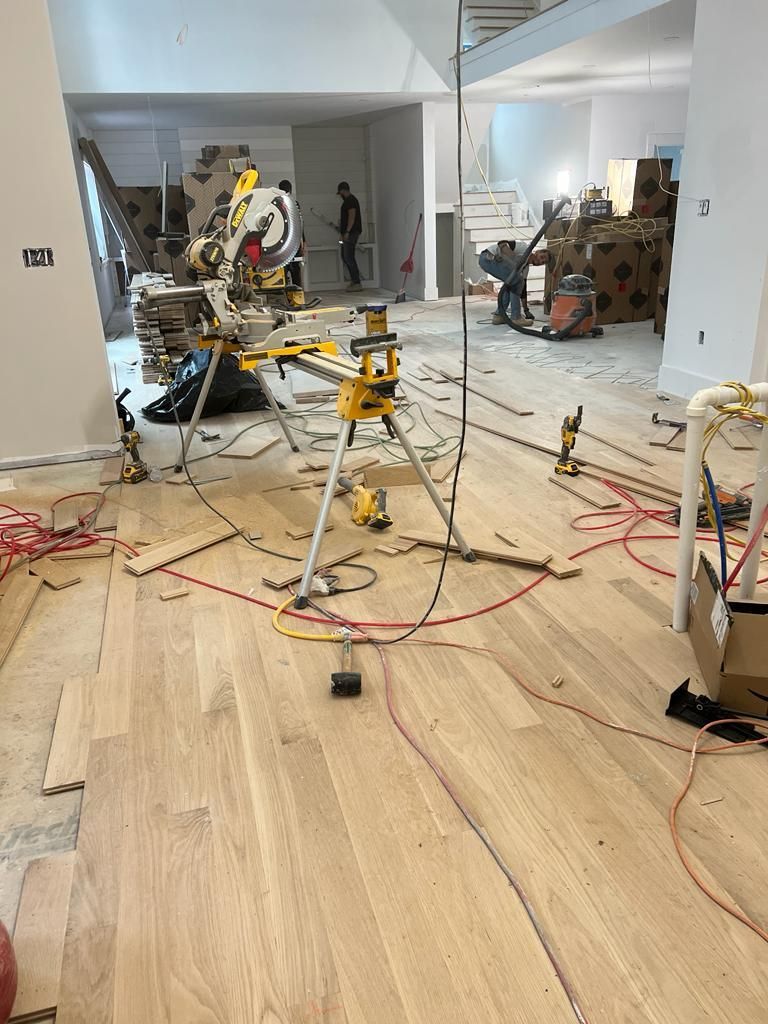 A construction site interior featuring a miter saw on a stand, scattered tools, and unfinished light hardwood flooring.