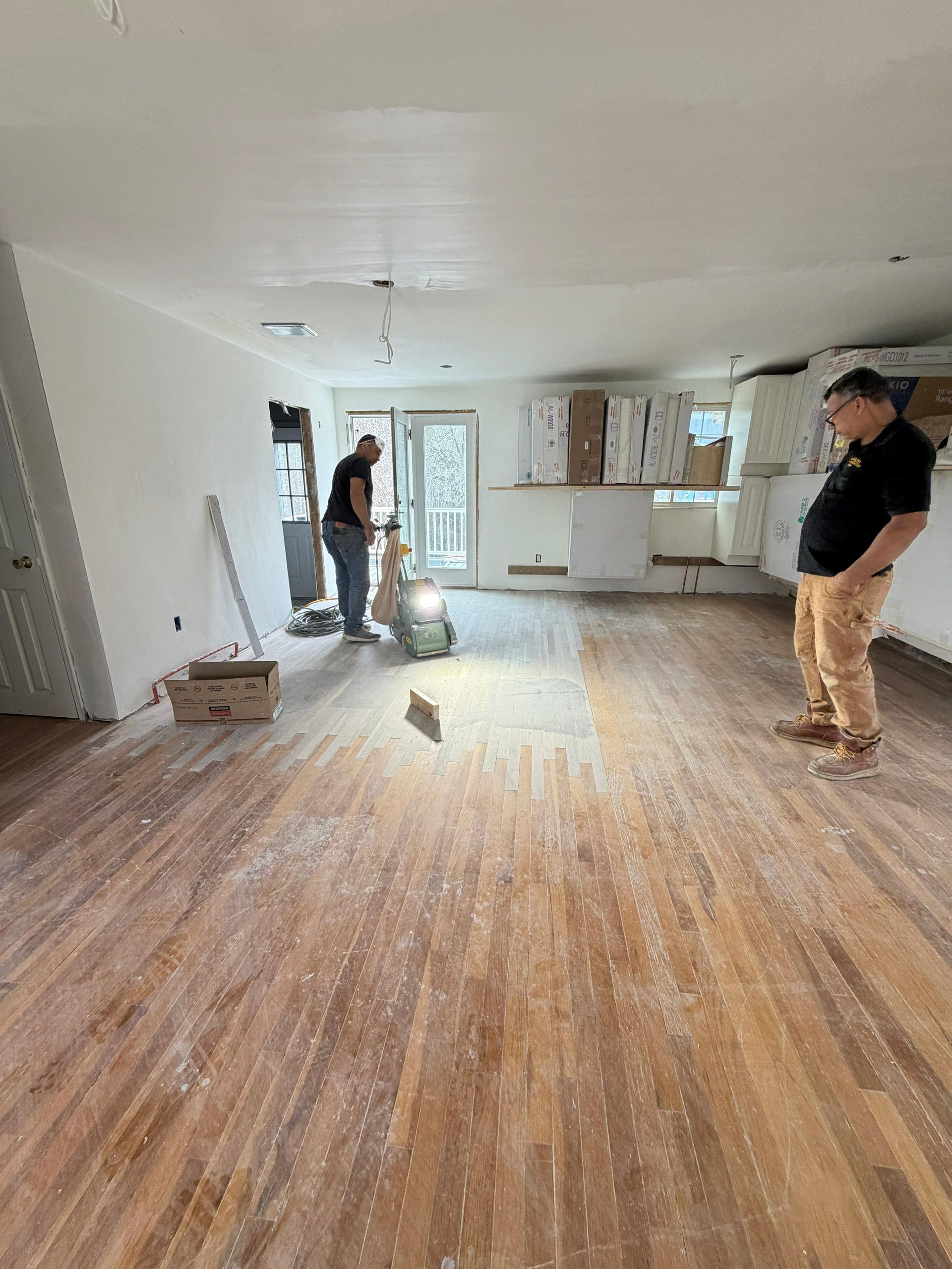 Two people work on sanding and refinishing wooden floors in a home renovation project.