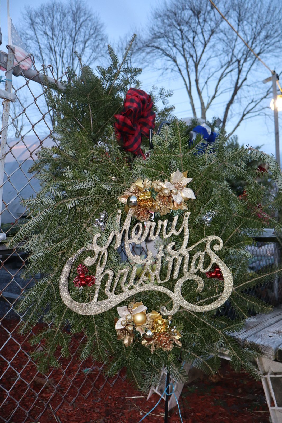 Christmas wreath on fence, Merry Christmas sign, red and gold accents, against a winter sky