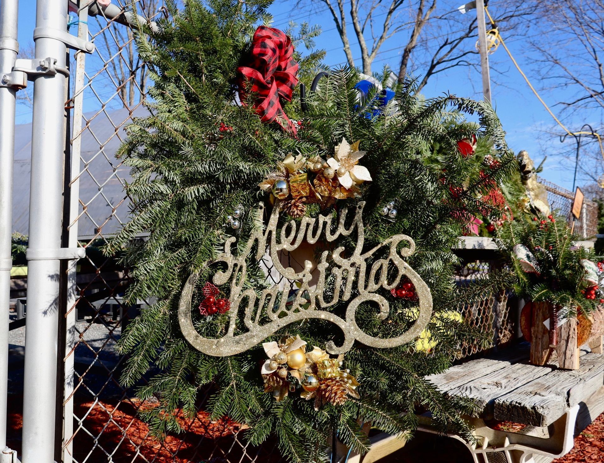 Christmas wreath on a fence, decorated with greenery, gold Merry Christmas sign, and red bow