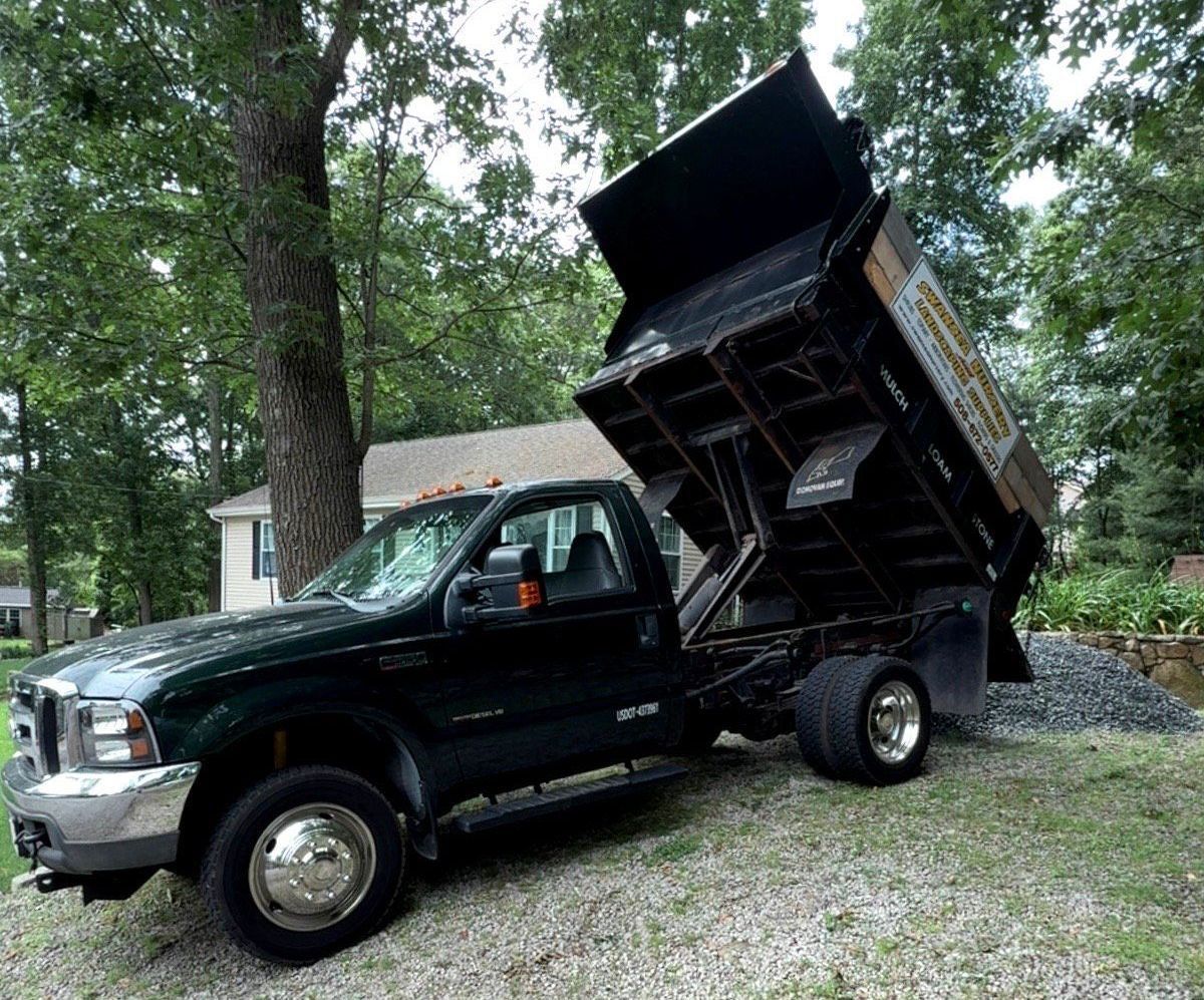 A dump truck with bed raised, unloading stones for landscaping