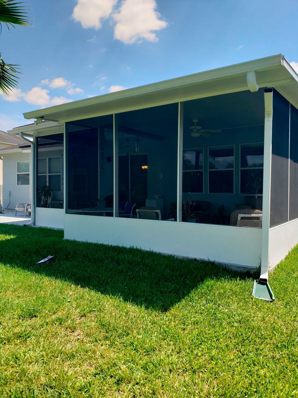 Screened-in patio with white trim, dark screens, and a low white wall. Green grass and blue sky.