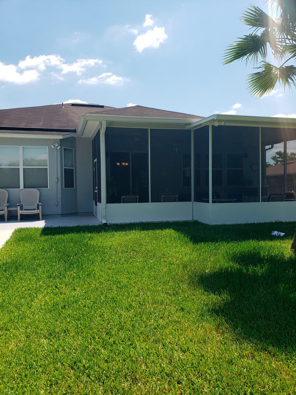 Backyard with green grass, patio, and screened-in porch under a bright sky.