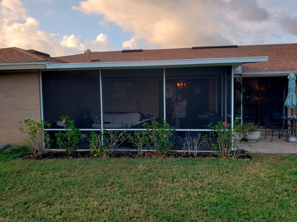 Screened patio with dark screens, white frame, plants, and a partial view of a home's interior.