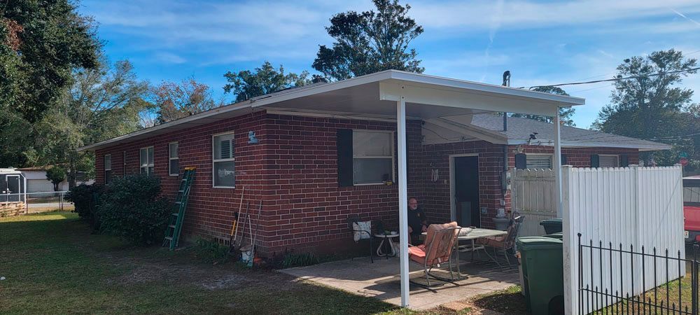 Brick building with a white awning, patio furniture, and a fence on a sunny day.