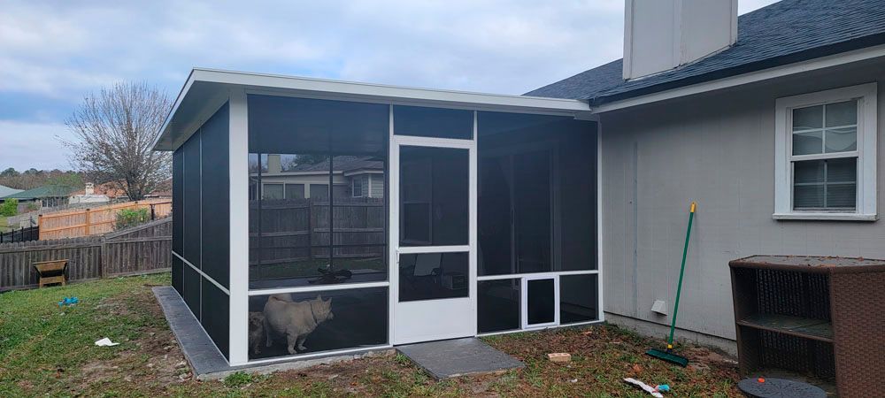 A screened-in porch attached to a light gray house. A dog is visible inside the porch.