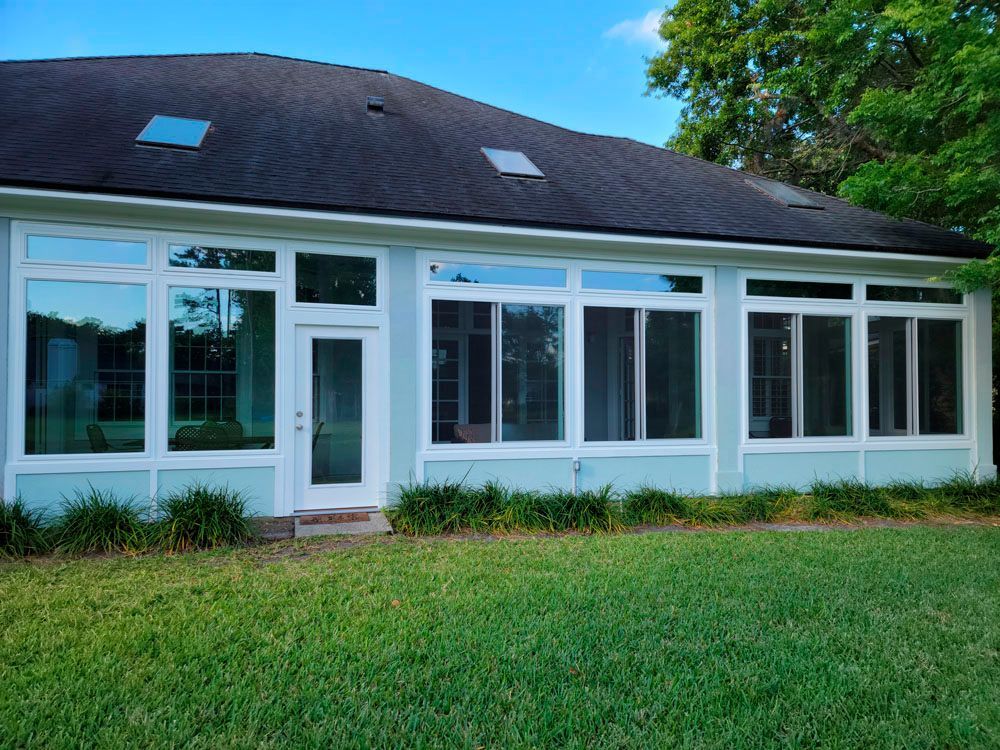 Light blue sunroom with large windows, white frames, and a dark roof, surrounded by green grass.