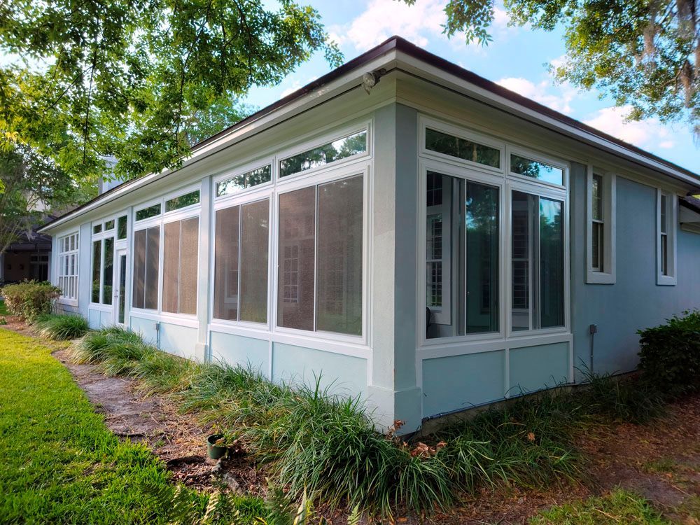 Light blue house with white-framed windows, surrounded by green grass and trees.