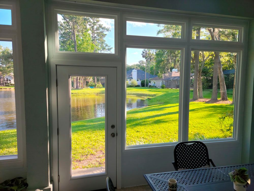 Sunroom with view of a pond, door and windows with white frames, green grass, and trees.