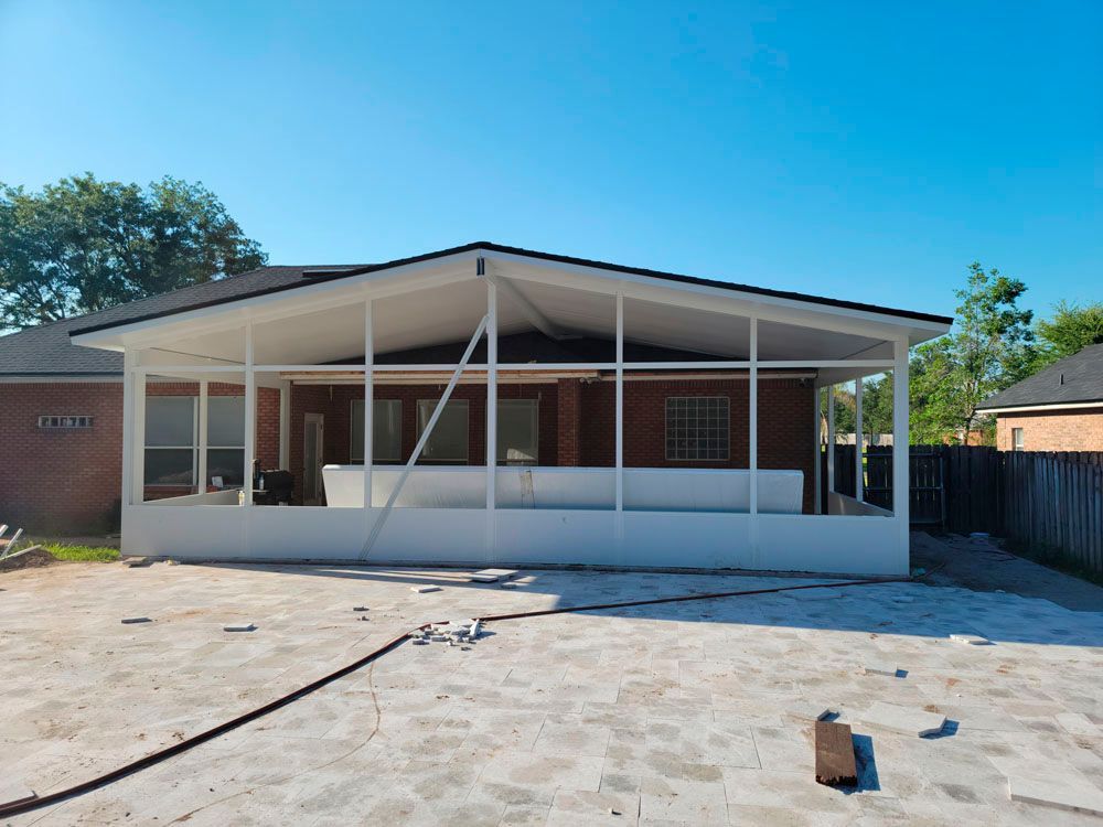 Screened patio attached to a brick house with white trim. Clear sky overhead, unpaved ground in foreground.