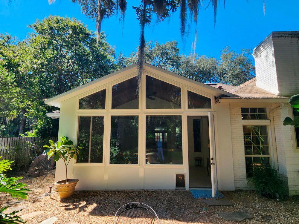 White sunroom with large windows, open door, and chimney on a sunny day.