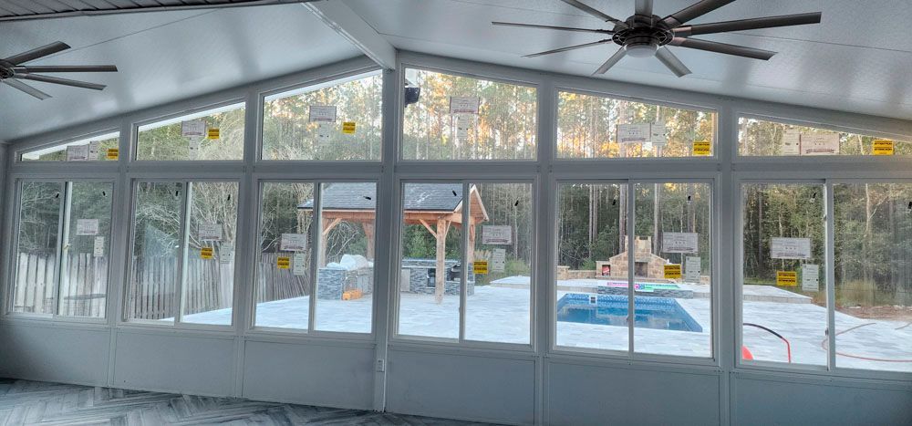 Sunroom with large windows overlooking a pool, patio, and forest.