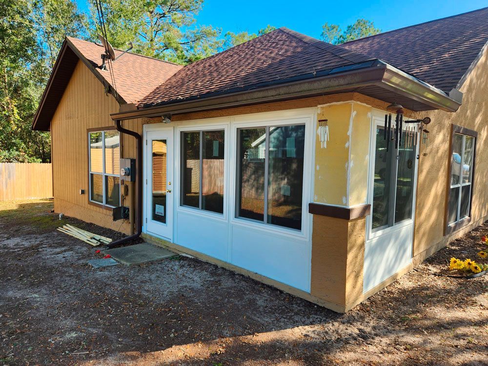 Tan house with brown roof, and white-framed windows on a sunny day.