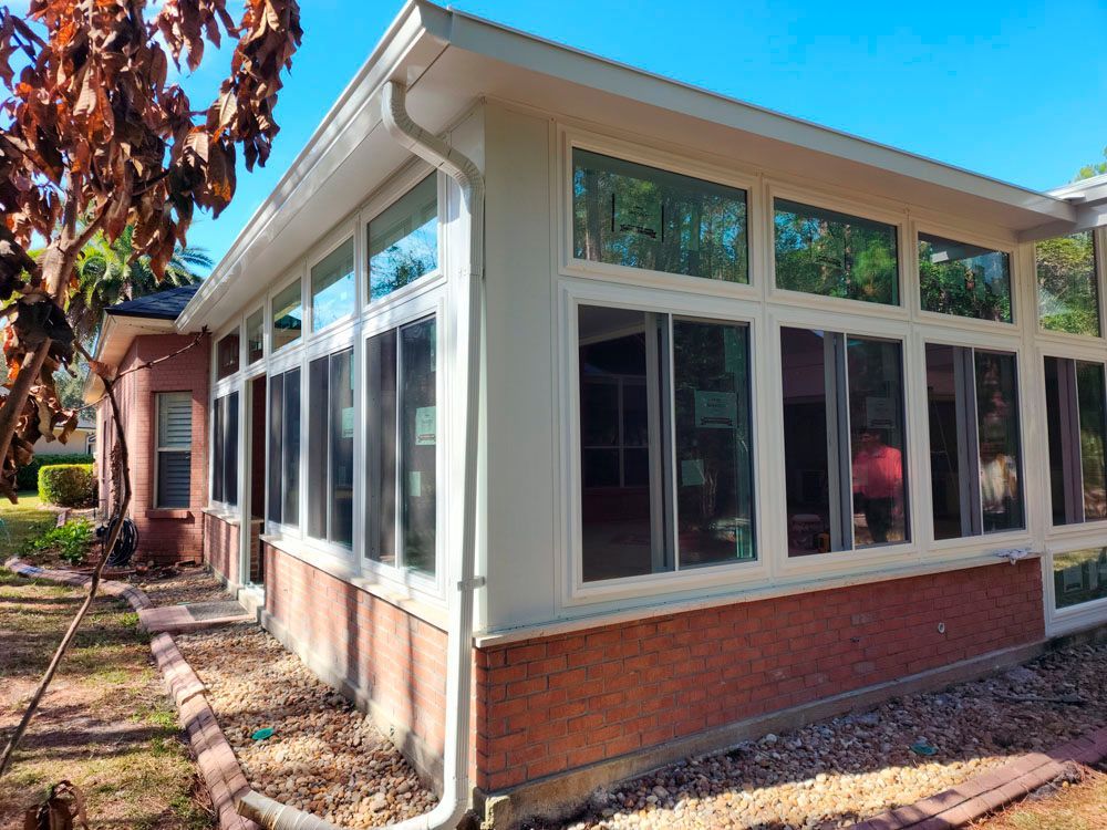 Sunroom with large windows, brick base, and white trim against a blue sky.