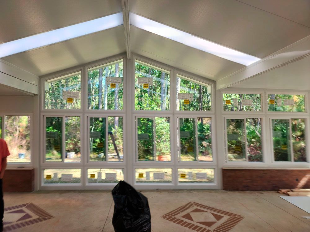 Sunroom interior with large windows overlooking trees. White ceiling and trim, tiled floor.