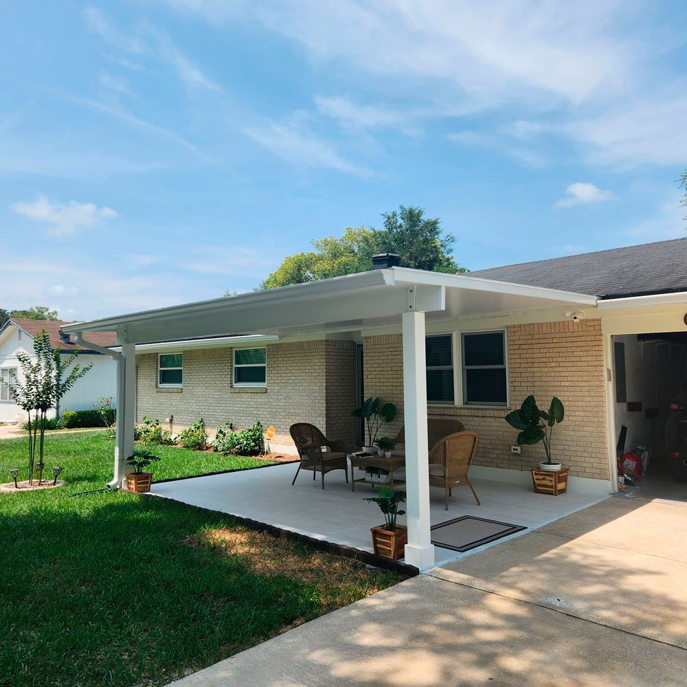 White patio cover attached to a light brick house with seating, plants, and a driveway.