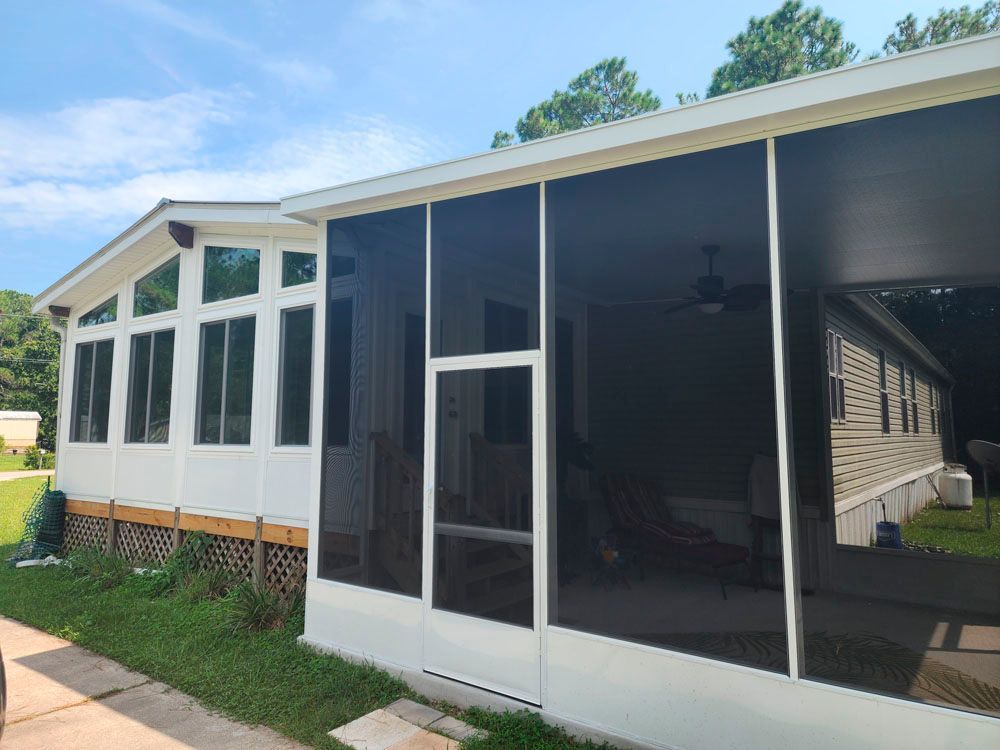 Screened porch attached to a white mobile home on a sunny day.