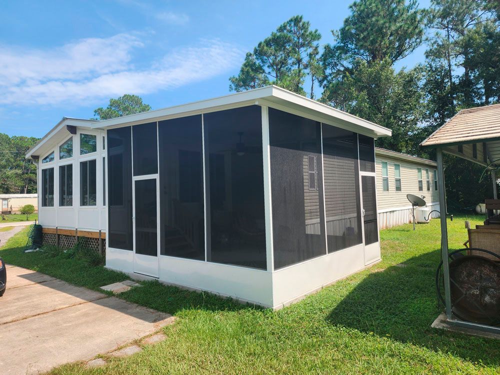 Screened-in porch attached to a white mobile home, with a concrete walkway and green grass.