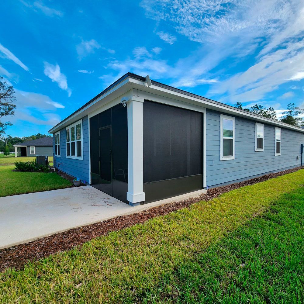 Blue house exterior with screened porch, white trim, and a concrete patio on a sunny day.