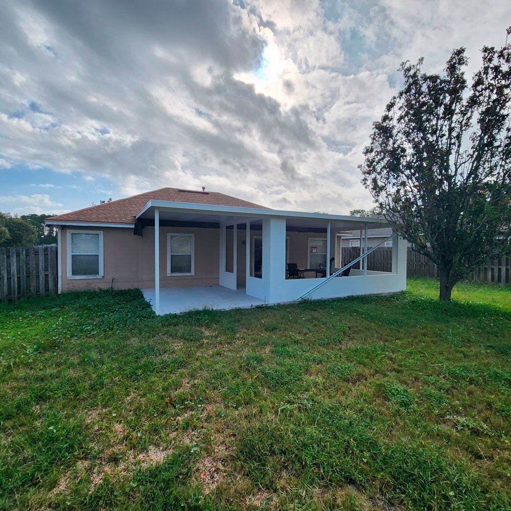 Backyard of a house with a screened-in patio and a grassy lawn under a cloudy sky.
