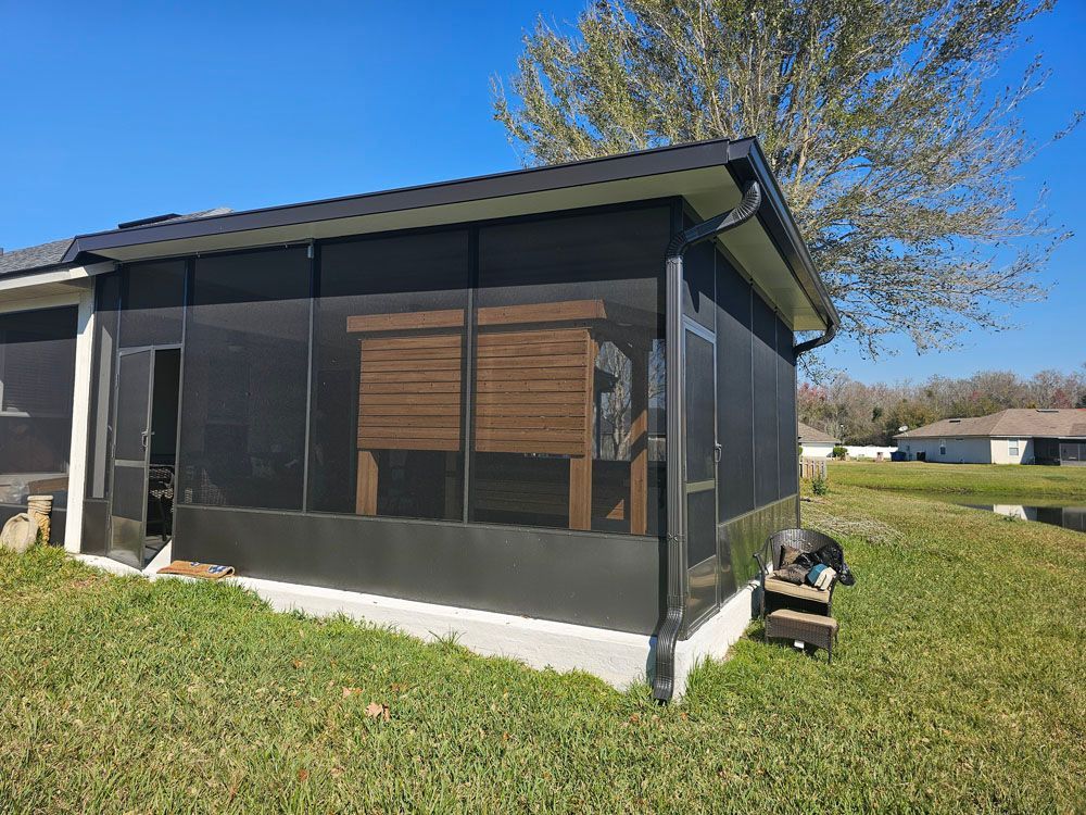 A screened porch with a brown structure inside, set on green grass under a blue sky.