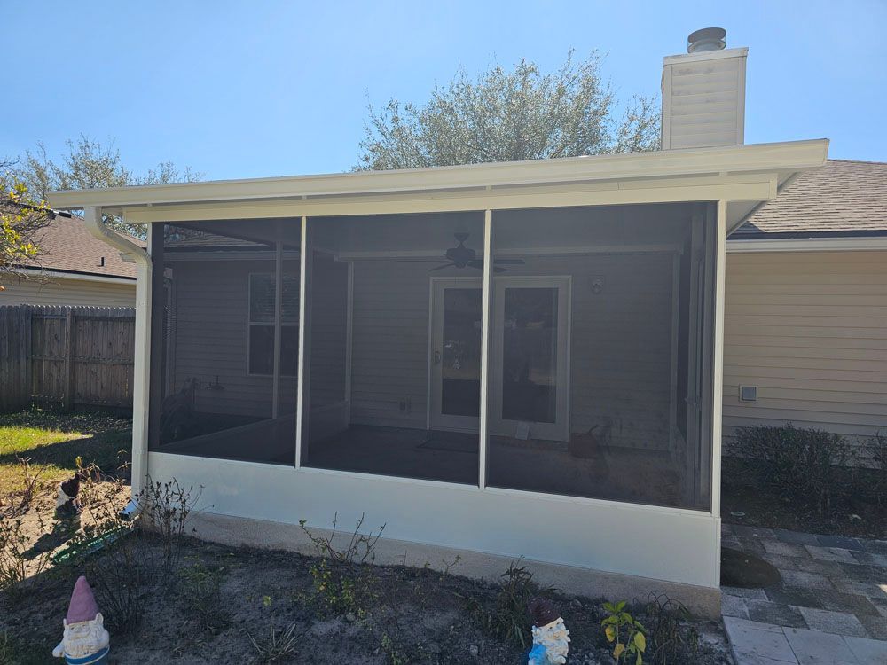 Screened porch attached to a house with a white frame and roof. Dark mesh screens enclose the space.