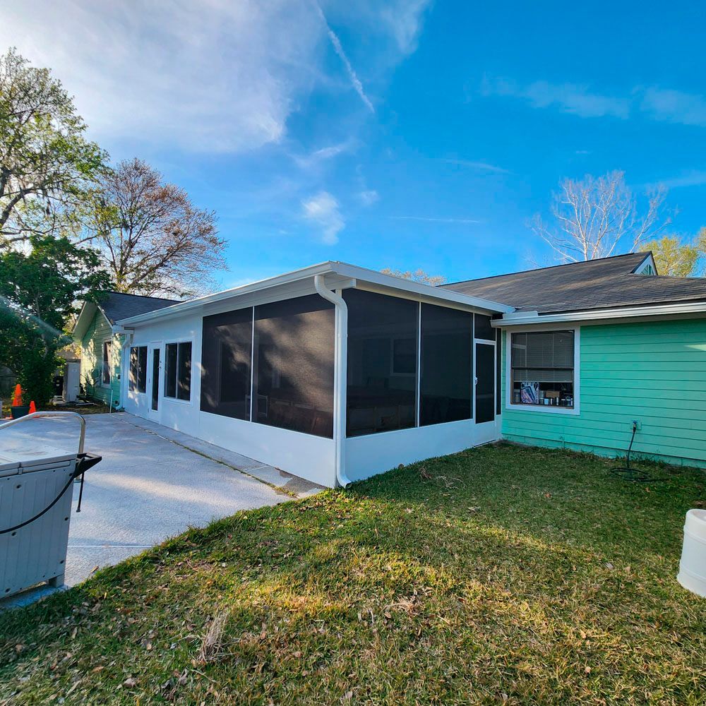 White screened porch attached to a turquoise house with a blue sky background.