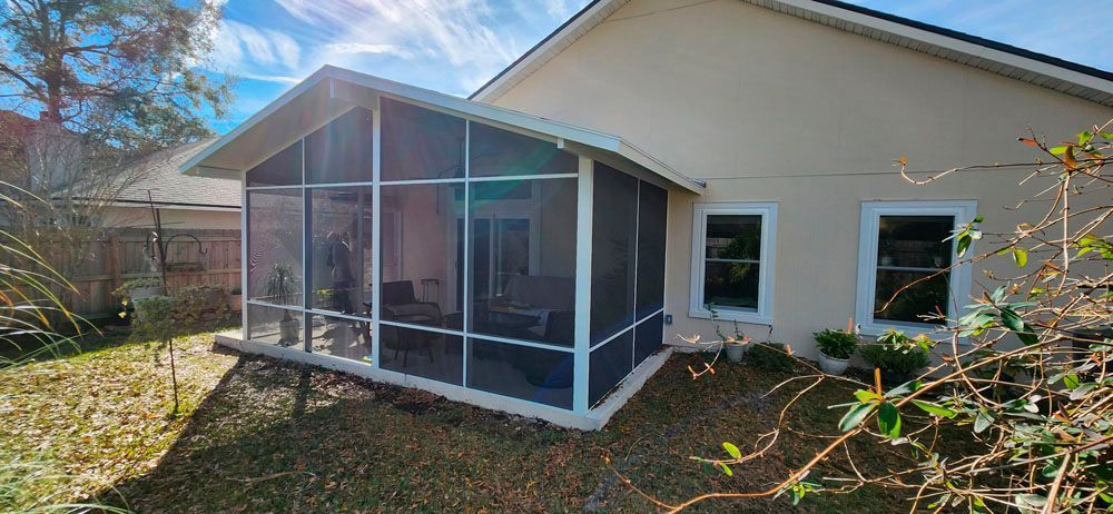 A screened porch attached to a beige house, blue sky visible.