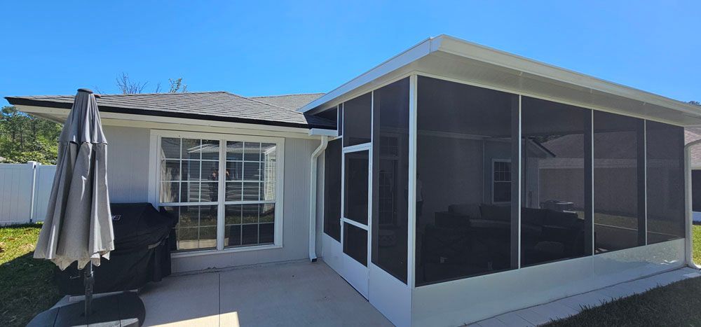 Exterior view of a house with a screened-in porch and patio area under a blue sky.