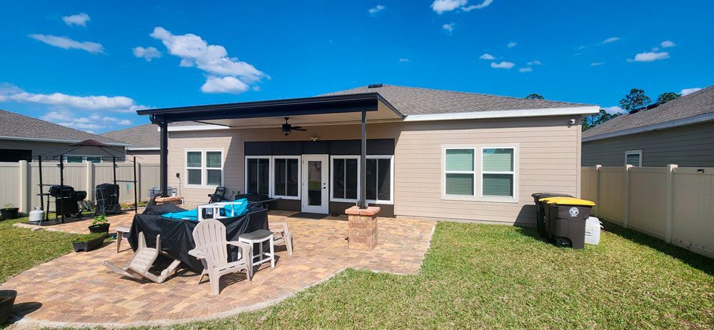 Backyard patio with a covered seating area, brick pavers, green grass, and blue sky.