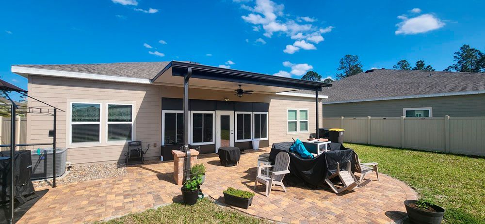 Backyard patio with a covered seating area and a beige fence, under a bright blue sky.