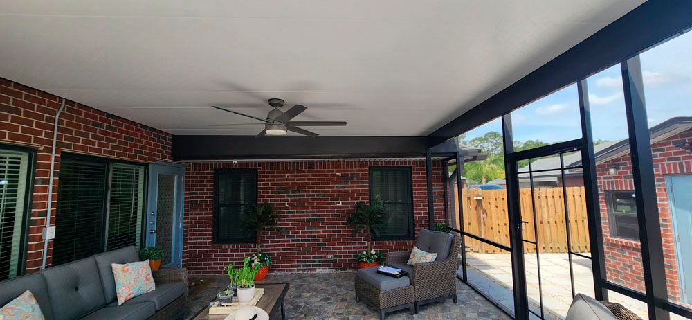 Screened-in patio with brick wall, ceiling fan, and outdoor furniture.