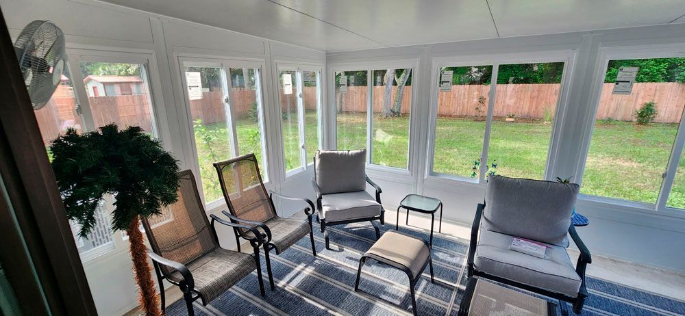 Sunroom with chairs, rug, windows, and a view of a backyard.
