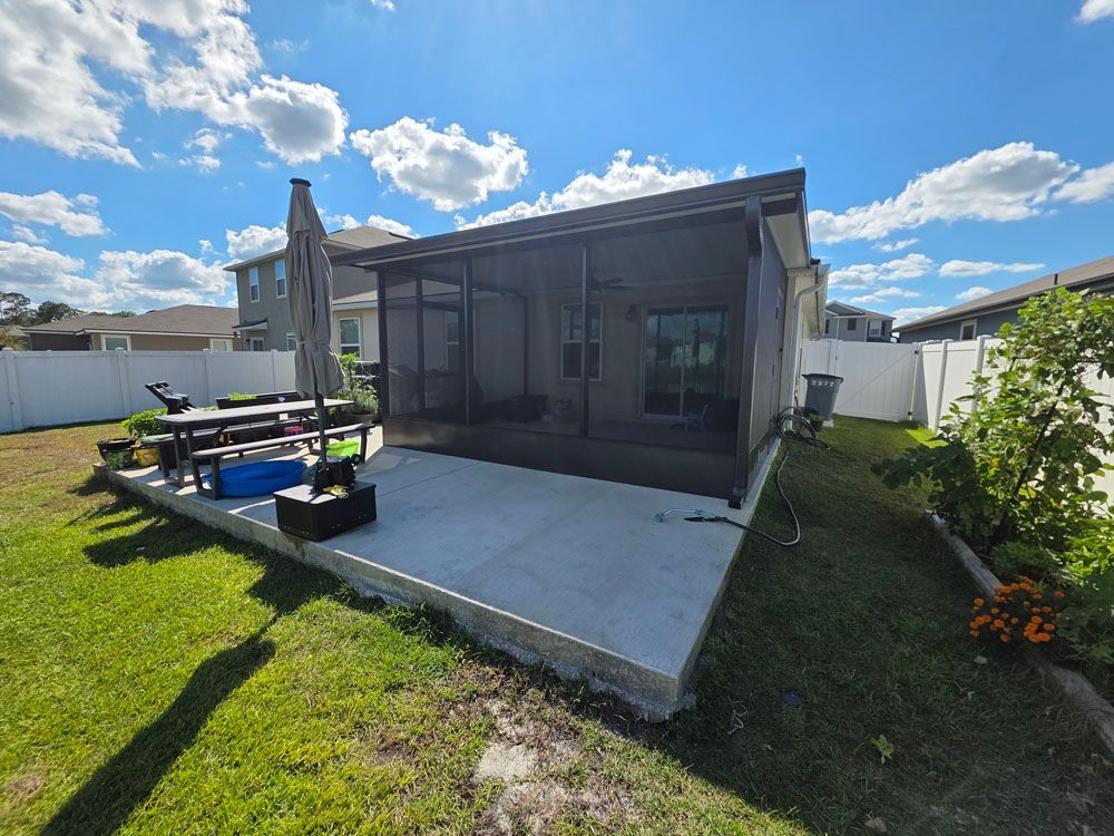 Backyard patio with a screened enclosure, concrete slab, table, umbrella, and surrounding grass.