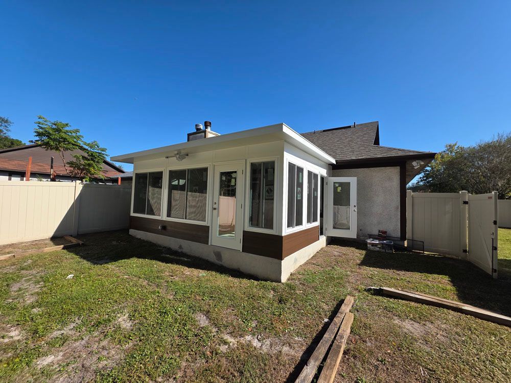 Backyard view of a white and brown sunroom addition with a blue sky.