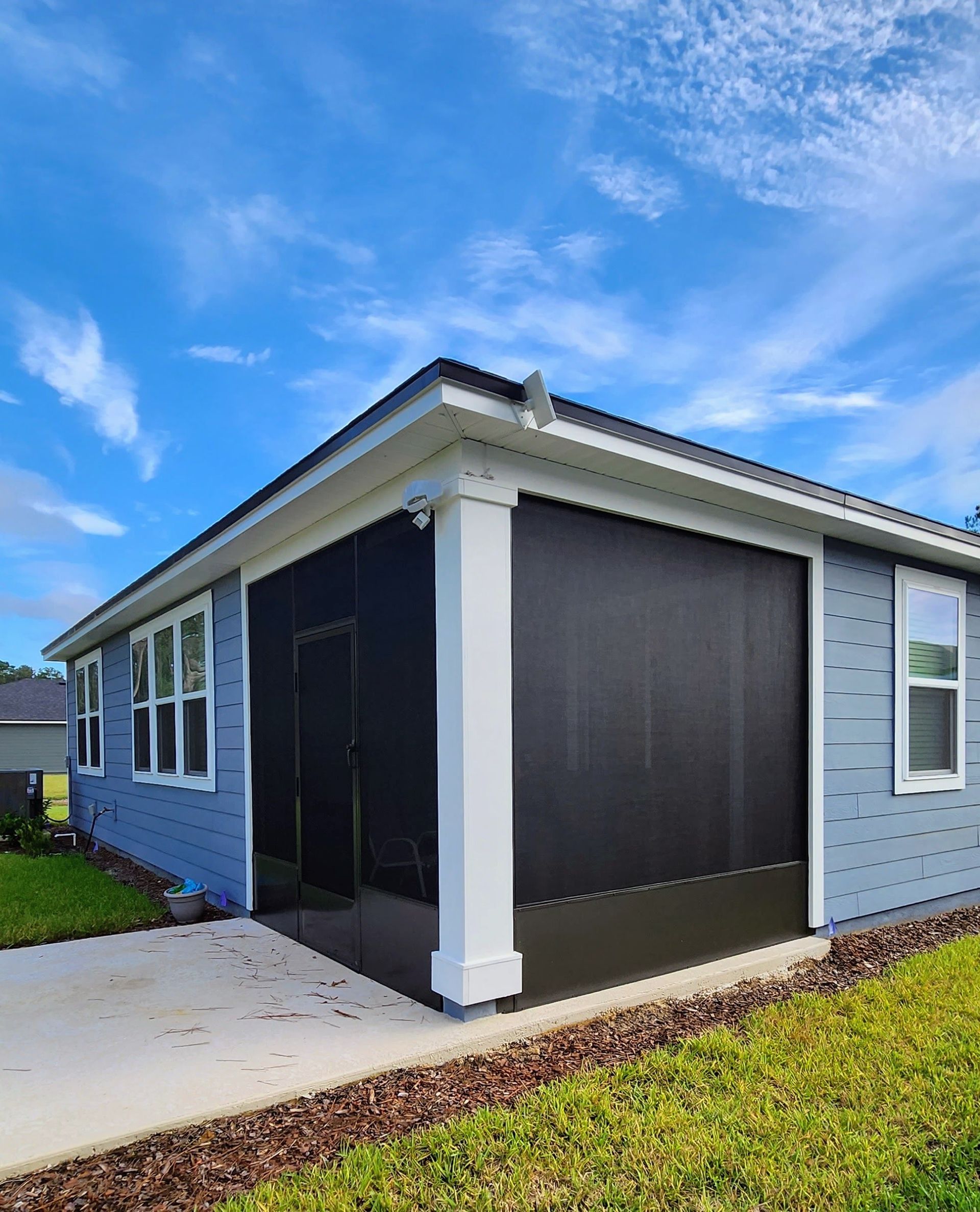 A low-angle view of a blue house corner with a black-screened-in patio area and a white support column under a blue sky.