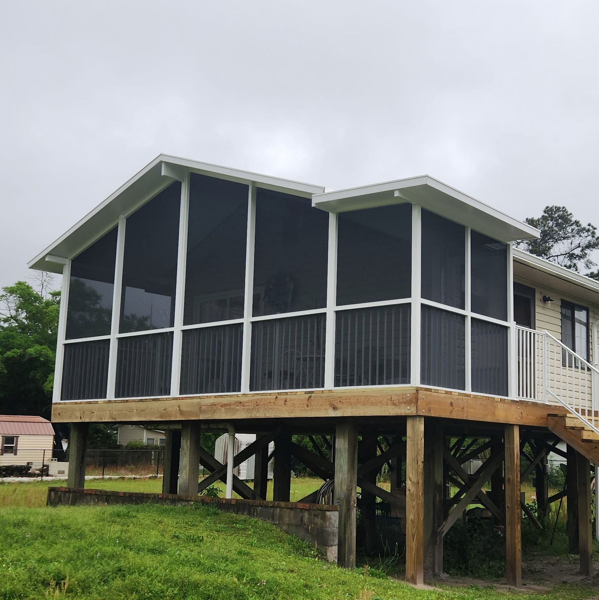 A white house with a raised, screened-in porch on wooden pilings set against a cloudy sky.