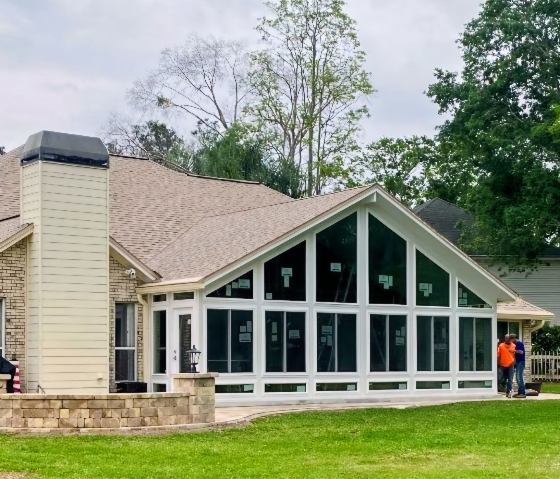 A newly constructed sunroom addition with large white-framed windows attached to the rear of a brick home.