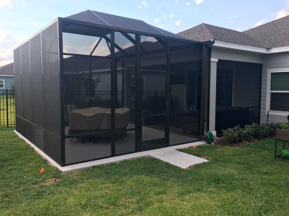 Dark screen enclosure on a concrete slab in a backyard with a dining set inside.