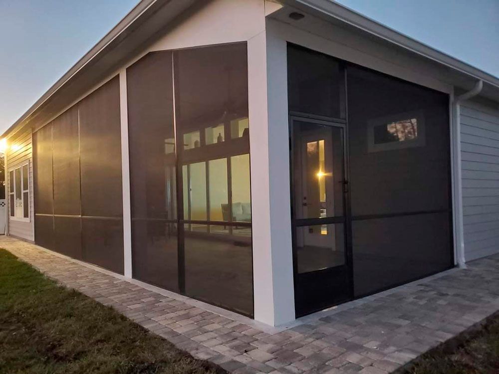 Screened-in porch attached to a house. Black screens, white trim, brick pavers, and a door are visible.