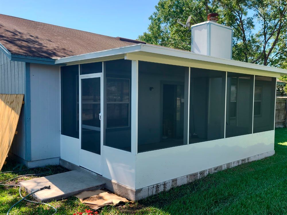 White-framed screened porch attached to a light blue house, with a chimney. Green grass surrounds it.