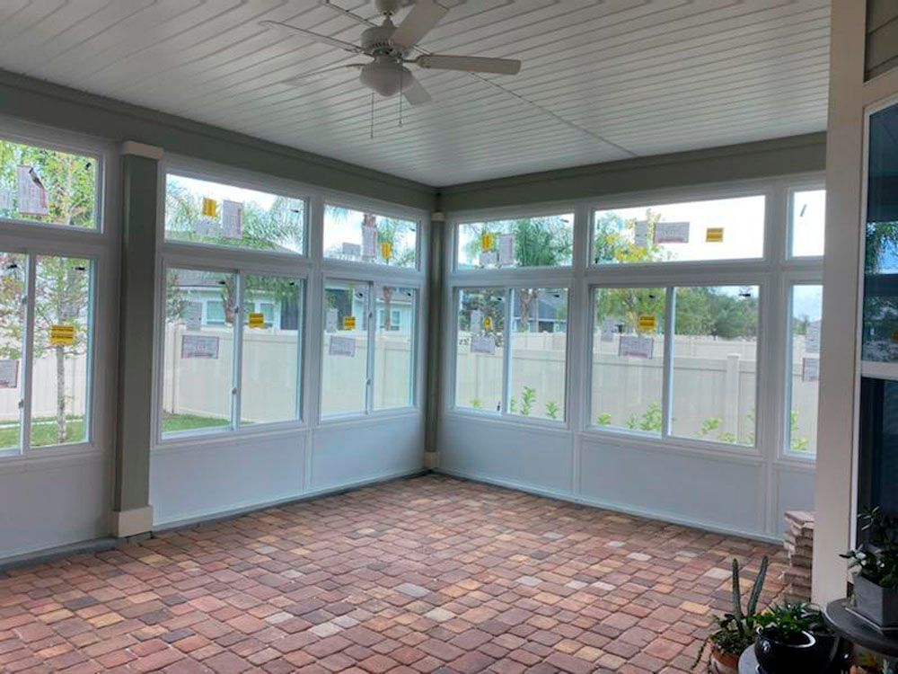 Sunroom with white-framed windows, brick floor, white ceiling, and a ceiling fan. View of a backyard through the windows.