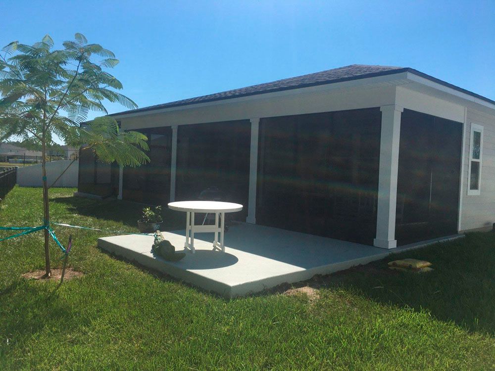 A backyard patio with dark screens, a small white table, and a small tree on the lawn.