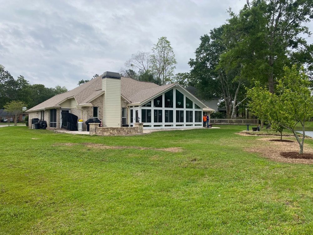 Tan house with large windows, chimney, and lawn under cloudy sky.