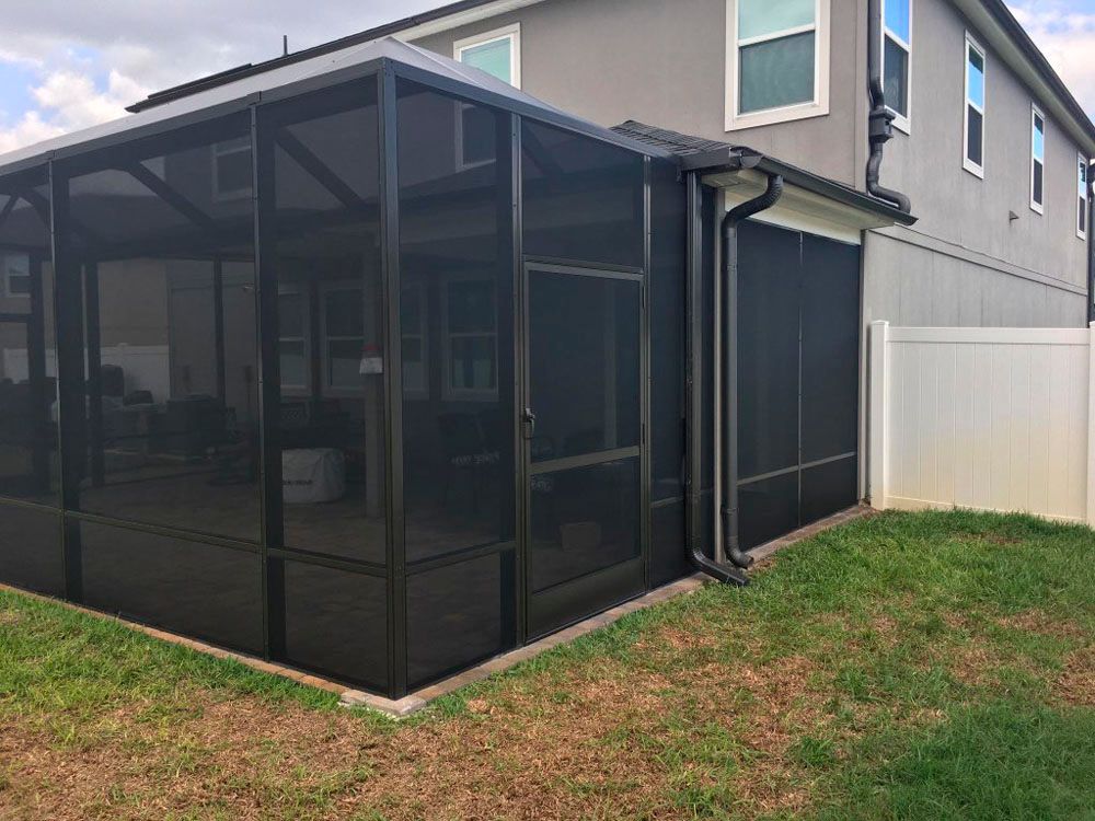 Black screened-in patio attached to a two-story beige house with a white fence on a grassy lawn.