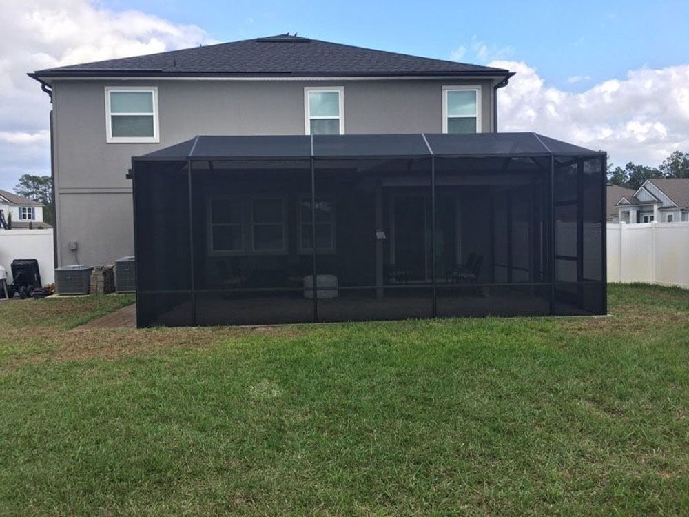 Backyard of a house with a black screened-in porch on the grass. Gray siding, blue sky.