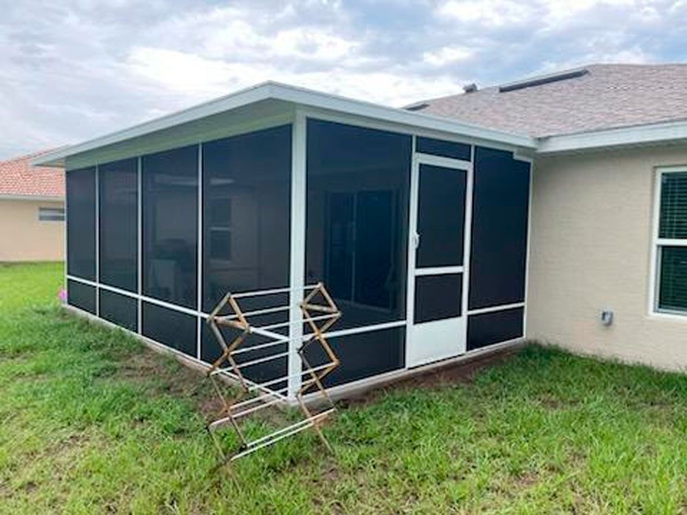 Screened-in porch attached to a tan house with white trim. A clothes drying rack stands in the grass.